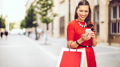 Kobieta w czerwonej sukience na zakupach, z telefonem w dłoni