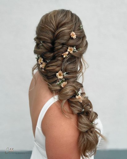 Objętościowy splot wykonany na długich włosach. Swobodnie rozłożone, drobne kwiatki podkreślają charakter boho fryzury.