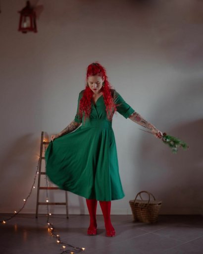 Rozkloszowana sukienka w kolorze zielonym z dodatkiem czerwonych rajstop oraz obuwia w tym samym kolorze.